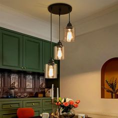 a kitchen with green cabinets and lights hanging from it's ceiling over a dining room table