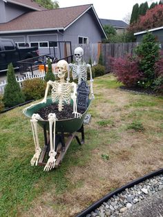 two skeletons are sitting in a wheelbarrow full of dirt and grass, outside