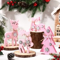 pink christmas decorations with snowflakes and deers on wooden stands next to pine cones