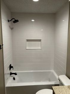 a white toilet sitting next to a bath tub in a bathroom under a ceiling light