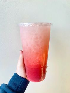 a hand holding up a pink and red drink in front of a white wall,