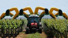 a tractor driving down a dirt road next to a bunch of green vines with inflatable arms