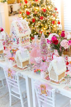 a table is decorated with gingerbread houses and pink flowers for a christmas party in front of a tree