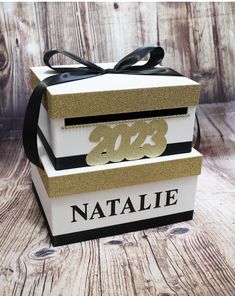 three stacked boxes decorated with gold glitter and black ribbon tied around the top one box says,'nattie '