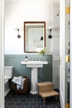 the bathroom is decorated in white and green with black tile on the floor, along with a wooden stool