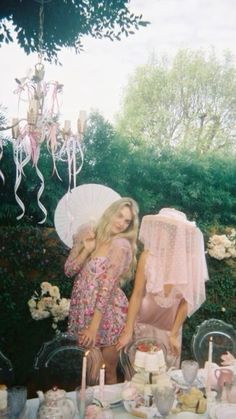 two women standing next to each other in front of a table with an umbrella and cake