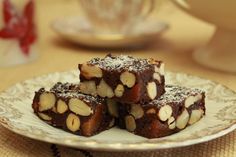 three pieces of brownie on a plate with nuts and powdered sugar around them