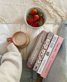 a bowl of strawberries next to books and a cup of coffee on a bed