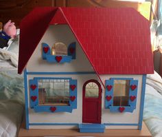 a doll house sitting on top of a bed next to a stuffed animal and window