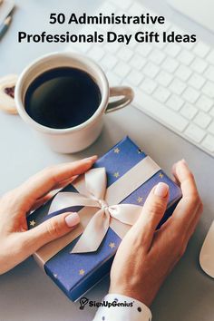 a person holding a blue gift box next to a cup of coffee on a desk