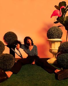 a woman sitting on the ground with scissors in front of her and plants behind her