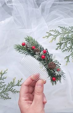 a person holding a comb with pine cones and berries on it in front of a veil