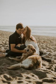 a man and woman kissing on the beach with their dog