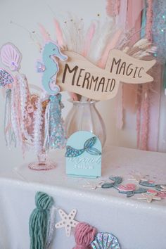 a table topped with a vase filled with pink and blue decorations next to a sign