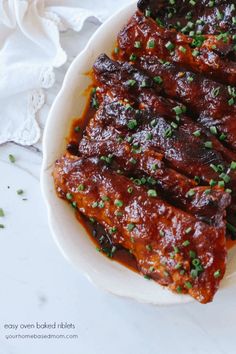 ribs covered in bbq sauce and garnished with scallions on a white plate