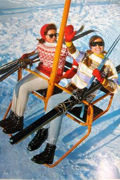 two people sitting on a ski lift in the snow with skis attached to them