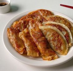 a white plate topped with sliced up food next to a cup of coffee and chopsticks