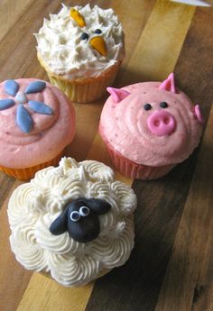 four cupcakes decorated with farm animals on top of a wooden table next to each other