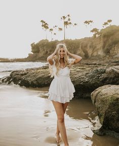 a woman standing on top of a sandy beach next to the ocean wearing a white dress