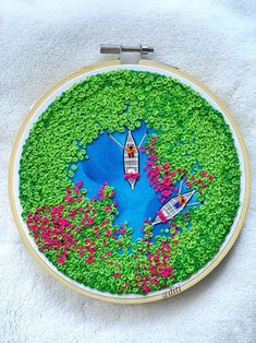 an embroidery project with two canoes in the water surrounded by green grass and pink flowers