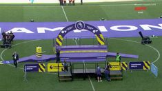 some people are standing on the sidelines in front of a purple and yellow sign