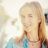 a blurry photo of a woman with long blonde hair wearing a blue shirt and necklace