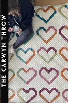 a woman is sitting on the floor next to a crocheted rug with hearts