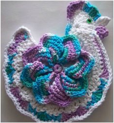 a crocheted flower is sitting on top of a white tablecloth with blue, purple and green accents