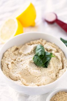 a white bowl filled with hummus next to sliced lemons