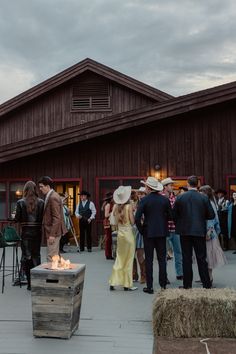 a group of people standing in front of a barn with a fire pit on the ground