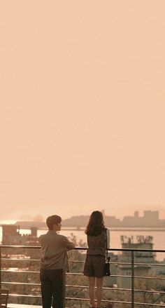 two people standing on a balcony looking at the water