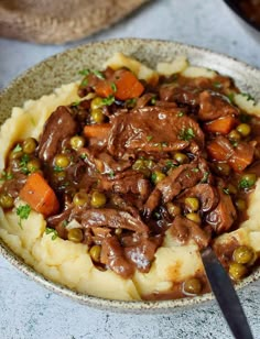 a bowl filled with meat and vegetables on top of mashed potatoes next to a fork