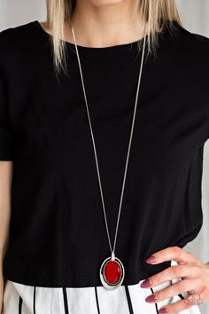 a woman wearing a black shirt and white skirt holding a red necklace with a circle pendant on it