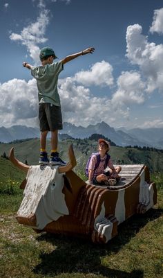 two boys are standing on top of a fake cow that is in the middle of a field