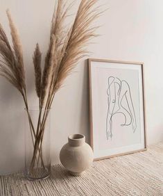 two vases with dry grass in them next to a framed nude drawing on the wall