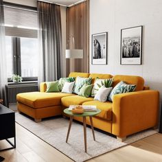 a living room with yellow couches and green pillows on the floor, next to a coffee table