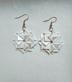 two white origami pieces are hanging from silver earwires on a white surface