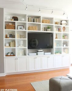 a living room with white bookcases and a flat screen tv on the wall