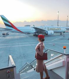 a woman walking down an escalator at an airport while another plane is on the tarmac behind her