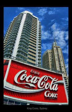 the coca - cola sign is in front of some high rise buildings and blue sky