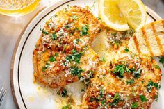 two pieces of chicken covered in parmesan cheese and garnished with herbs