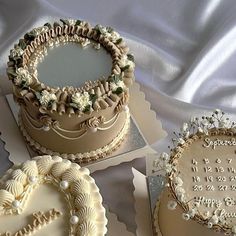 three decorated cakes sitting on top of a white cloth covered table next to each other