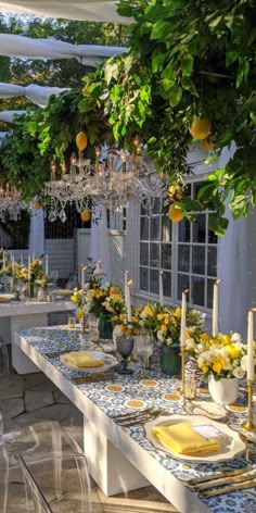 an outdoor dining area with yellow and white tableware, chandeliers and lemons hanging from the ceiling