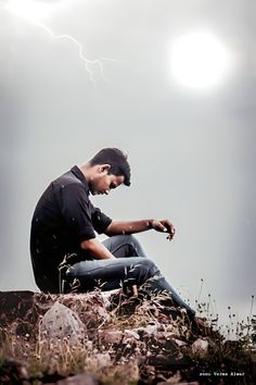 a young man sitting on top of a rock under a lightning storm in the sky