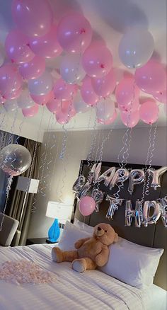 a teddy bear sitting on top of a bed under balloons