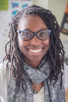 a smiling woman with glasses and a scarf around her neck is looking at the camera