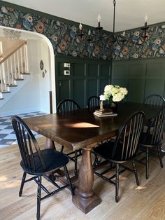 a dining room table with four chairs and a vase on top of it in front of a staircase