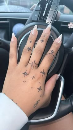 a woman's hand on the steering wheel of a car with stars tattooed on it