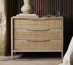 a white vase sitting on top of a wicker dresser next to a bed with pillows