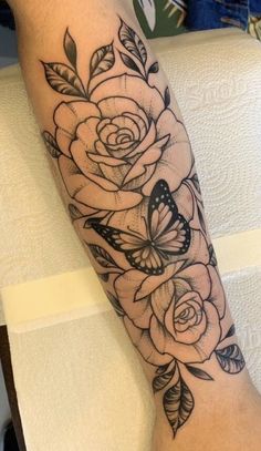 a black and white rose tattoo on the left arm with butterflies flying around it's petals